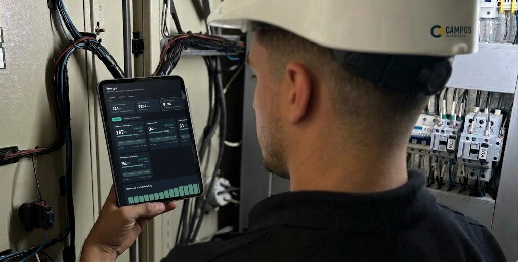 Técnico frente a un tablero eléctrico mirando en una tablet la pantalla de monitoreo de Campo